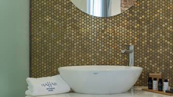 Un baño con un lavabo blanco, un espejo redondo y una pared con mosaico dorado.