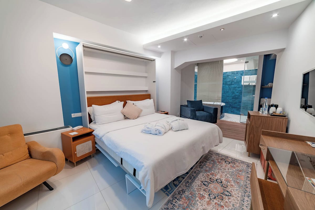 Una habitación de hotel moderna con cama, mesita de noche, silla, escritorio y zona de ducha.