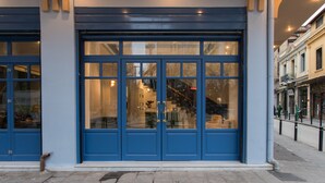 Un bâtiment à la façade bleue, doté de grandes fenêtres en verre et d’un escalier apparent menant à un étage supérieur.