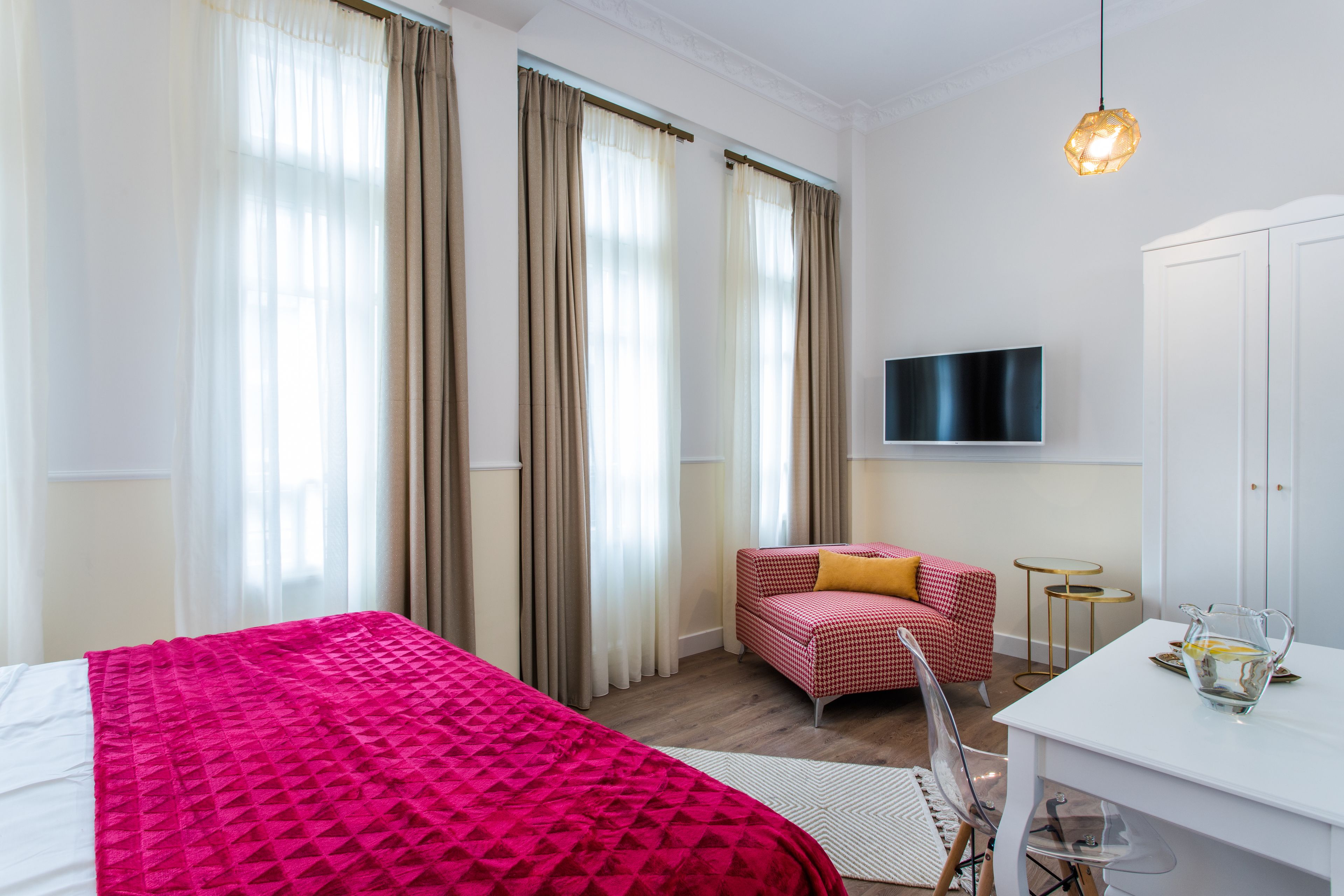 Ein Hotelzimmer mit einem großen Bett, einer kleinen Couch, einem Fernseher und einem Schreibtisch mit einer Karaffe Wasser.