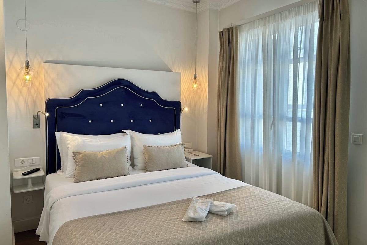 Una habitación de hotel con una cama grande, mesitas de noche y una ventana con cortinas.