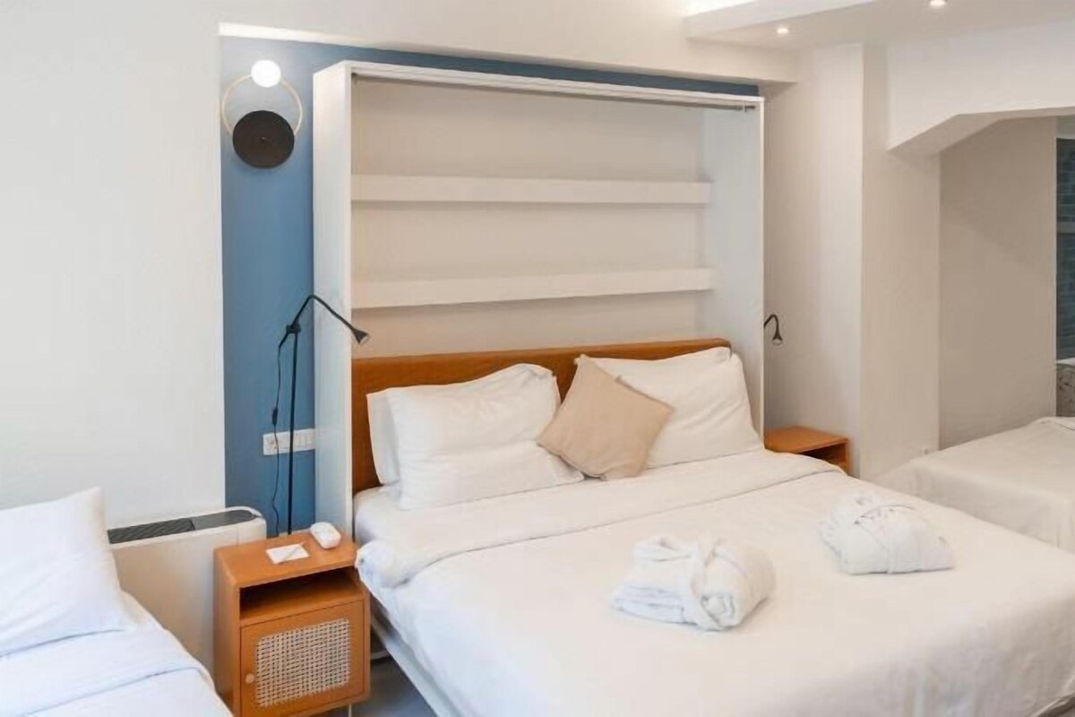 Een hotelkamer met twee bedden, een groot raam, een inloopdouche en een nachtkastje met een lamp.
