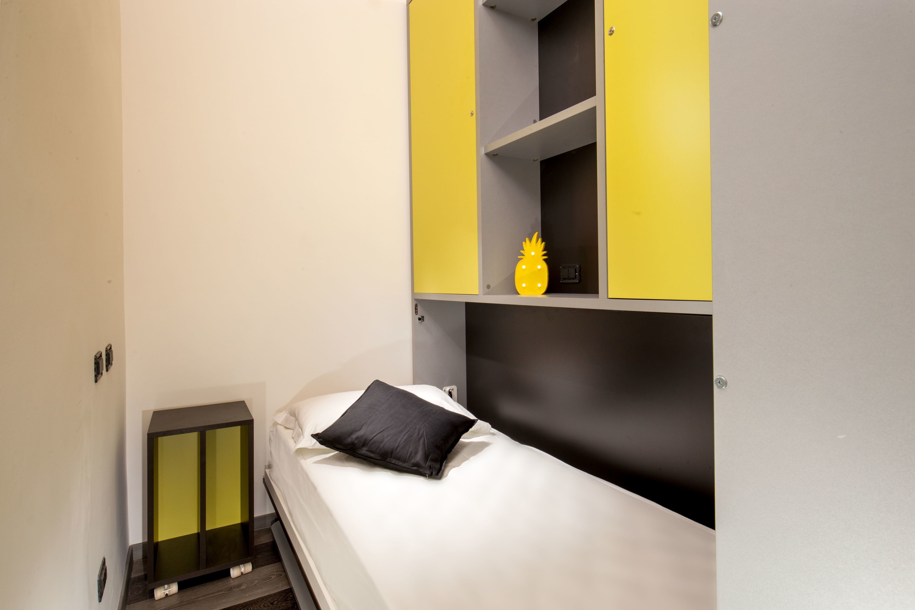 Un dormitorio pequeño y moderno con una cama, una mesita de noche y un estante empotrado con una piña decorativa.