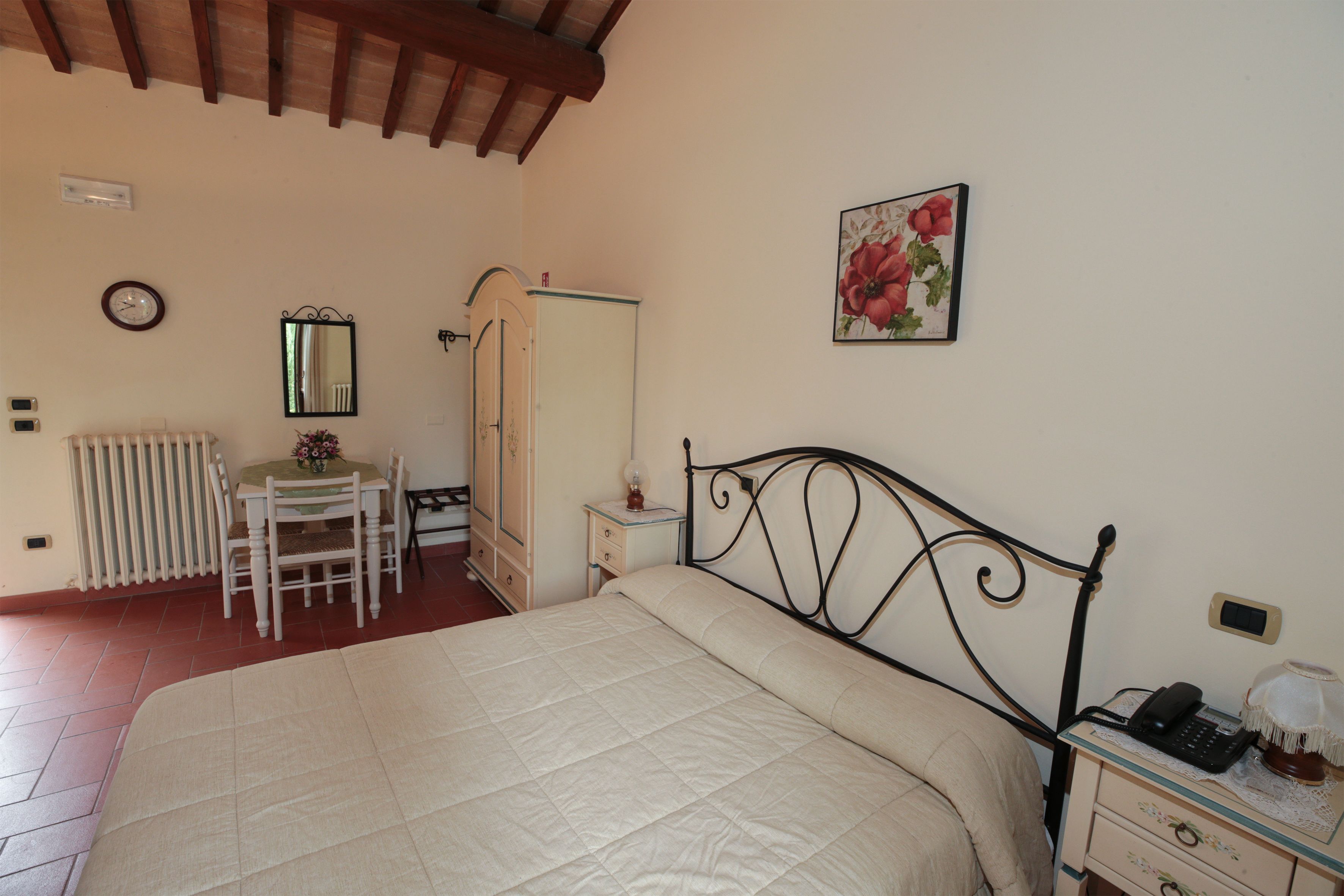 A bedroom with a bed, bedside table, dresser, chair, radiator, and a painting on the wall.