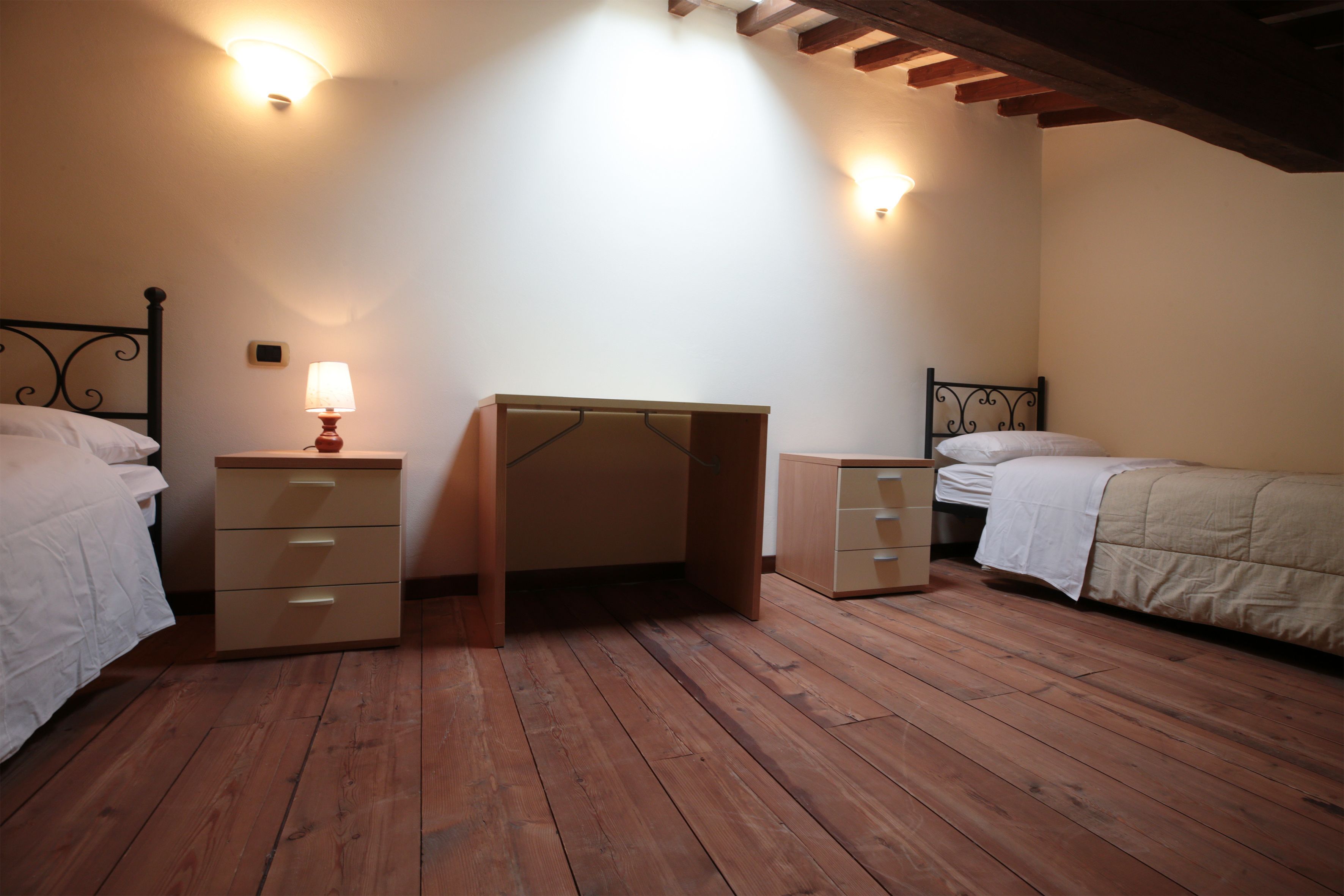 Quarto com duas camas, uma escrivaninha e uma mesa de cabeceira.