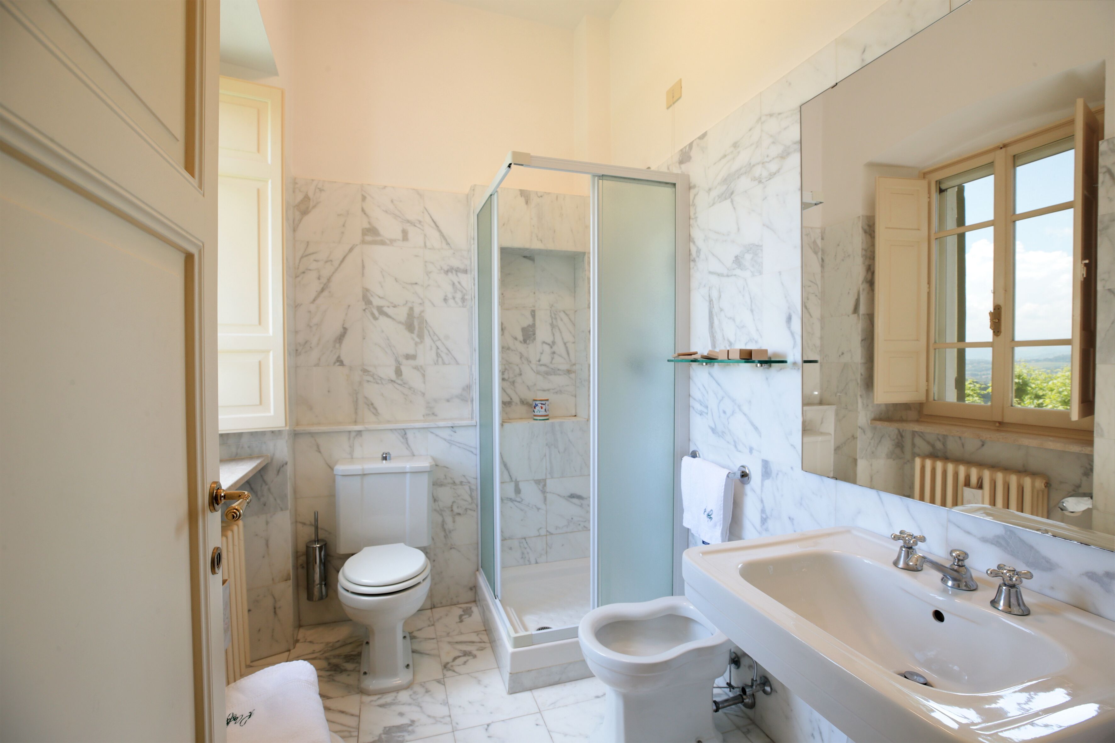 A bathroom with a toilet, bidet, glass shower enclosure, and a sink with a mirror.