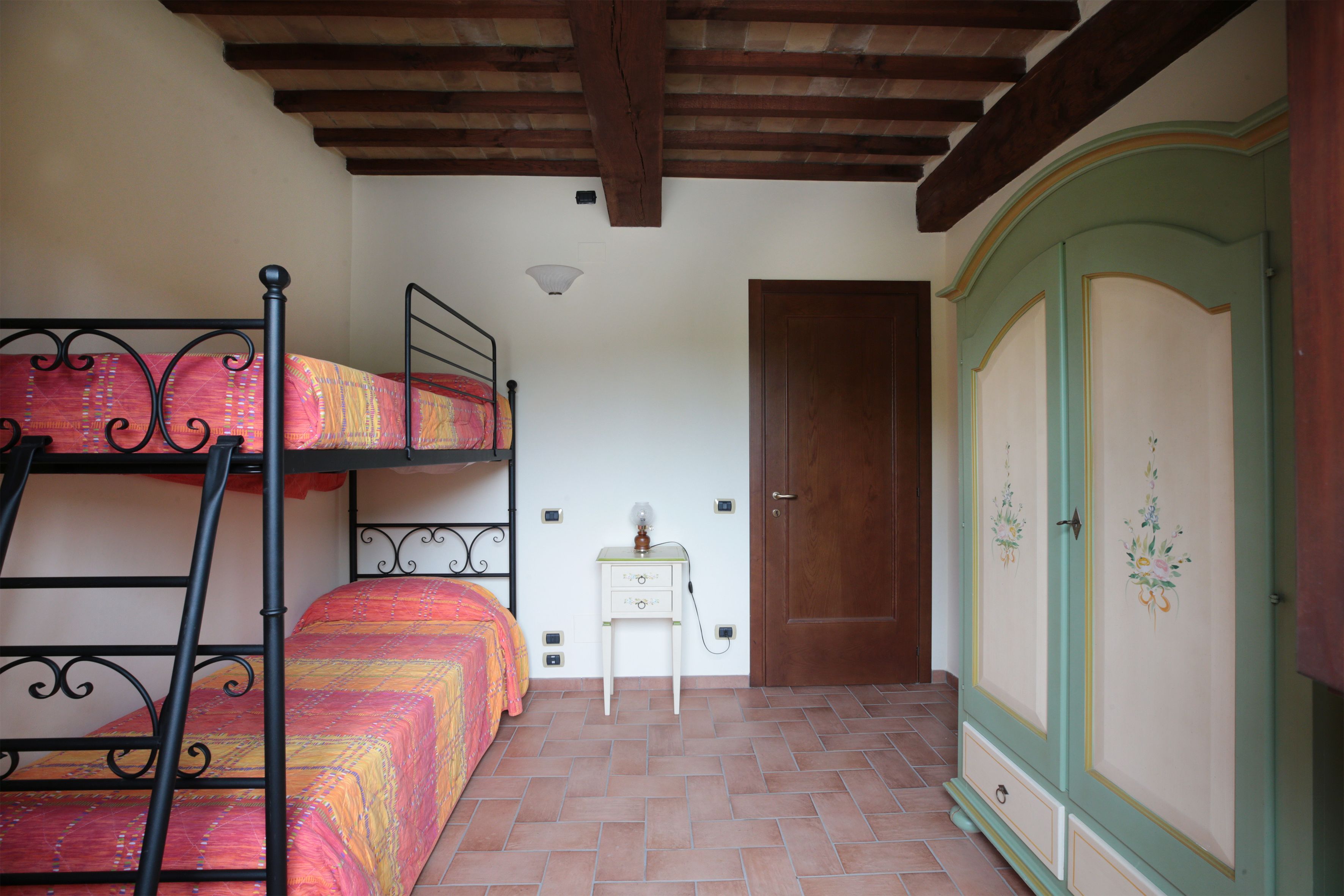 Une chambre avec des lits superposés, une table de chevet avec une lampe, une armoire et une porte.