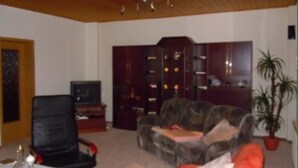 A living room with a wooden ceiling, a black leather chair, a patterned sofa, a television, and a bookshelf. - Ferienwohnung Müller (Spremberg)