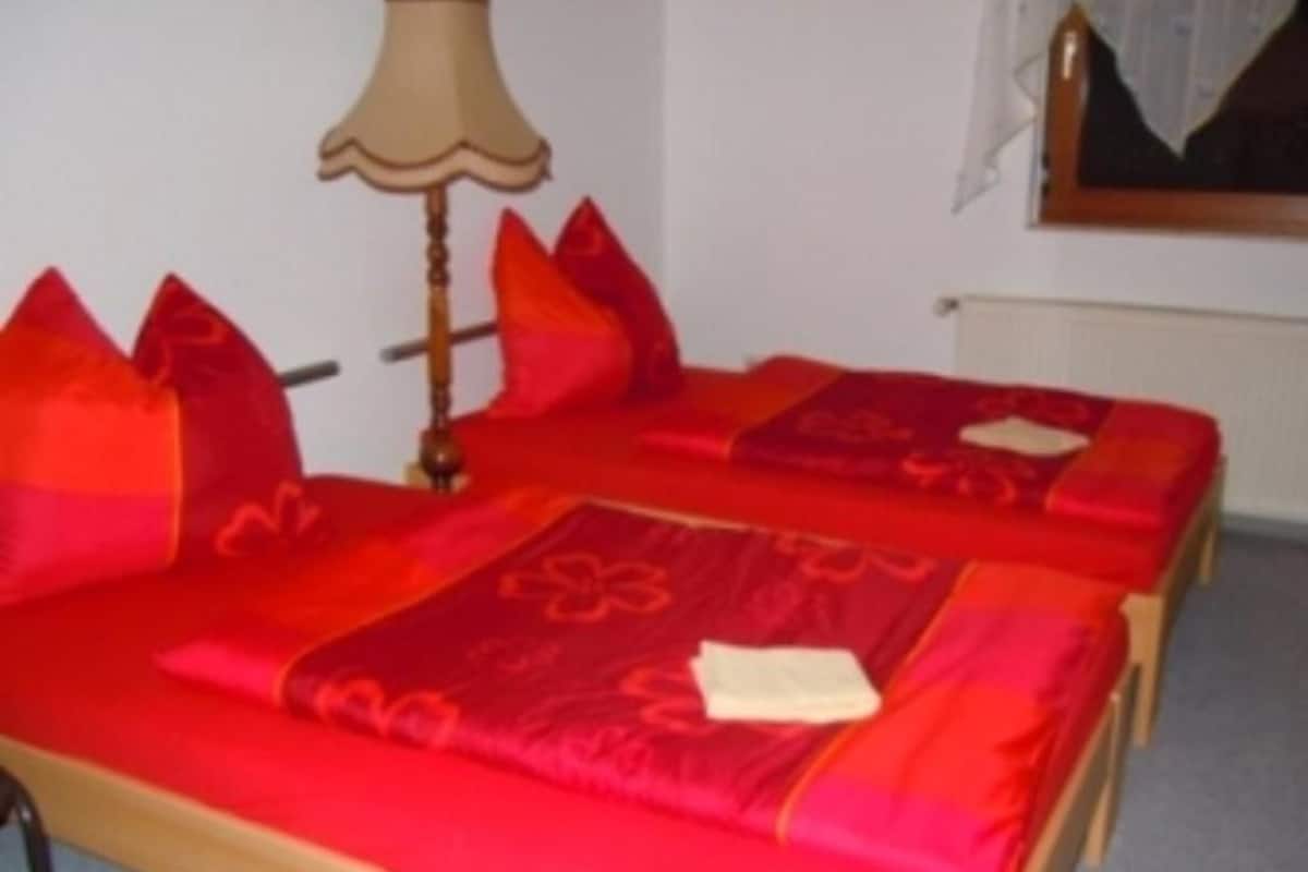 Une chambre d’hôtel avec deux lits, chacun doté d’une literie rouge et d’une tête de lit en bois. Une lampe se trouve sur le côté gauche de la pièce.
