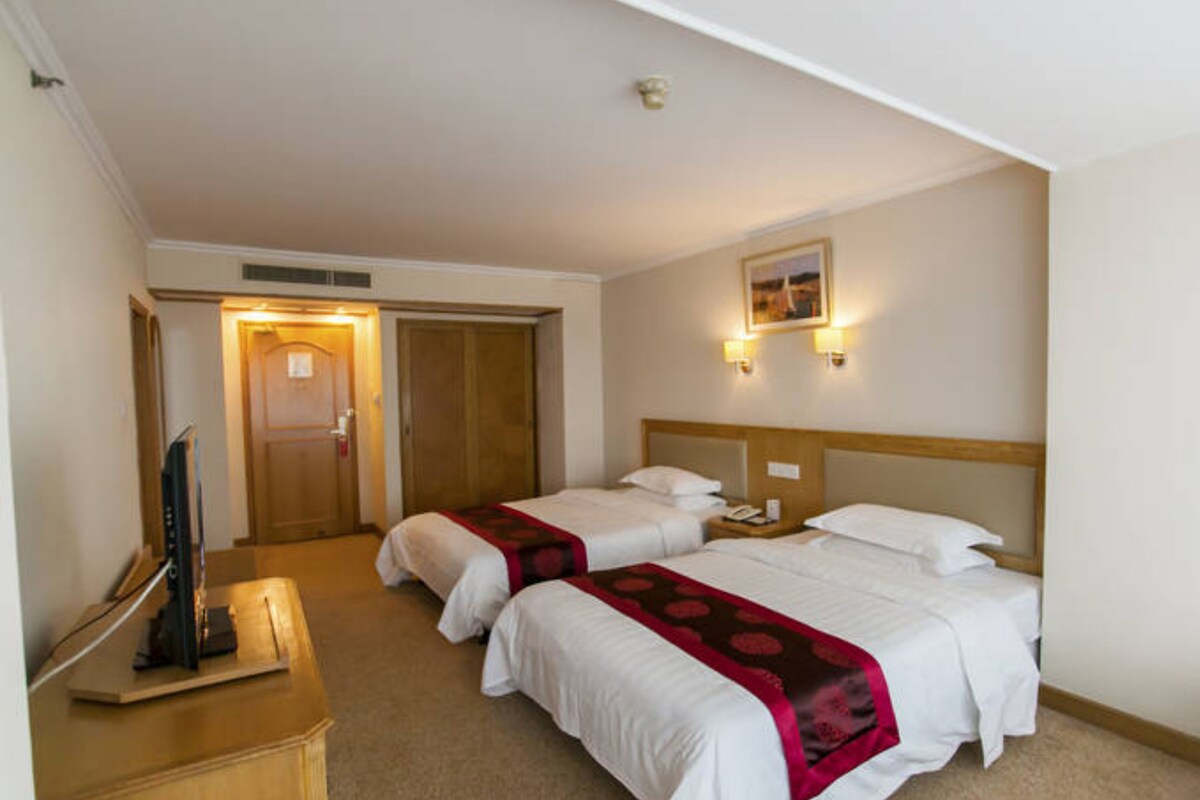 Een hotelkamer met twee bedden, een houten hoofdeinde, een bureau met een computer en een televisie.