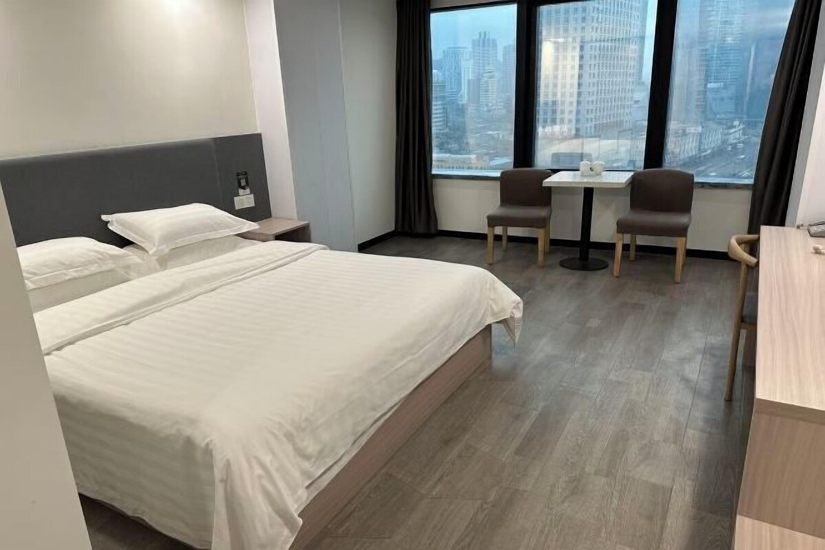 Een hotelkamer met een groot bed, een bureau, twee stoelen en een stadszicht door grote ramen.