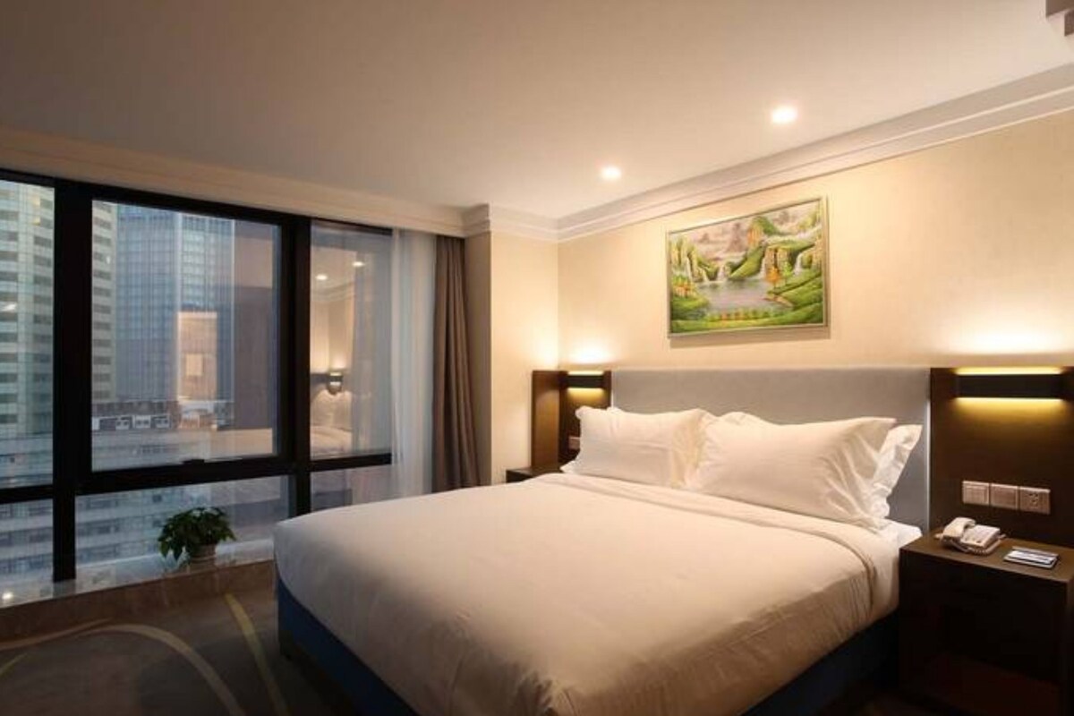 Een hotelkamer met een groot bed, een nachtkastje met een telefoon en een schilderij aan de muur.
