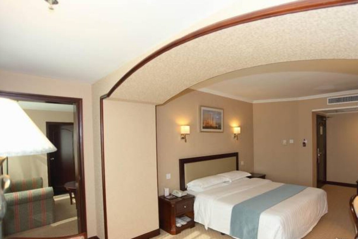 Een hotelkamer met een bed, nachtkastje, lamp en een spiegel.