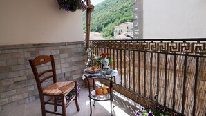 A balcony with a wicker chair, a small table with fruits and pastries, and a hanging flower basket.