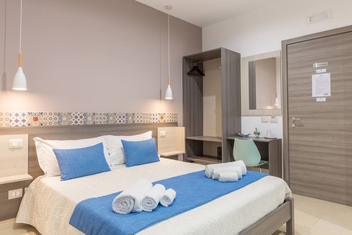 Habitación de hotel con cama bien hecha, escritorio, silla, armario y perchero.