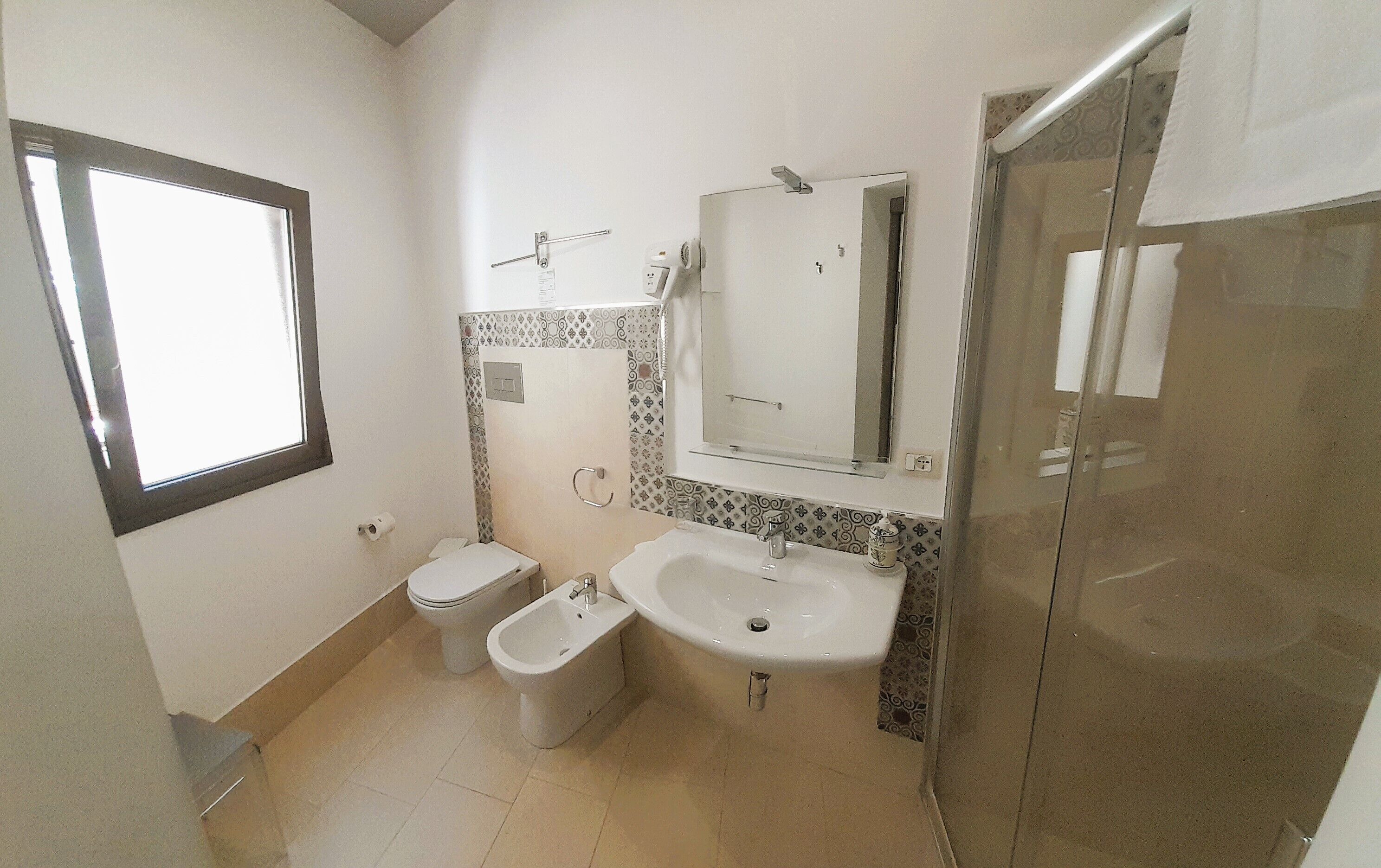 A small bathroom with a toilet, bidet, sink, and a glass shower enclosure.
