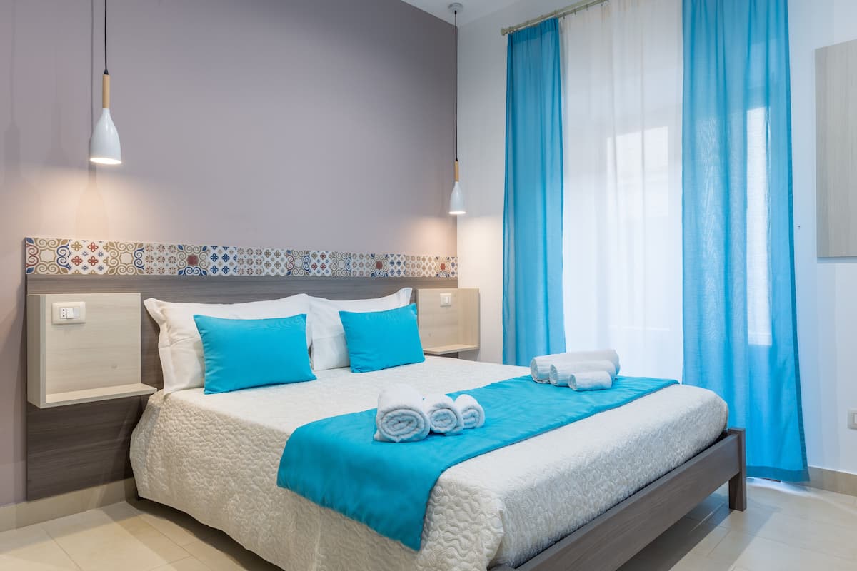 Una cama bien tendida con ropa de cama azul y blanca, un edredón azul y toallas enrolladas al lado.