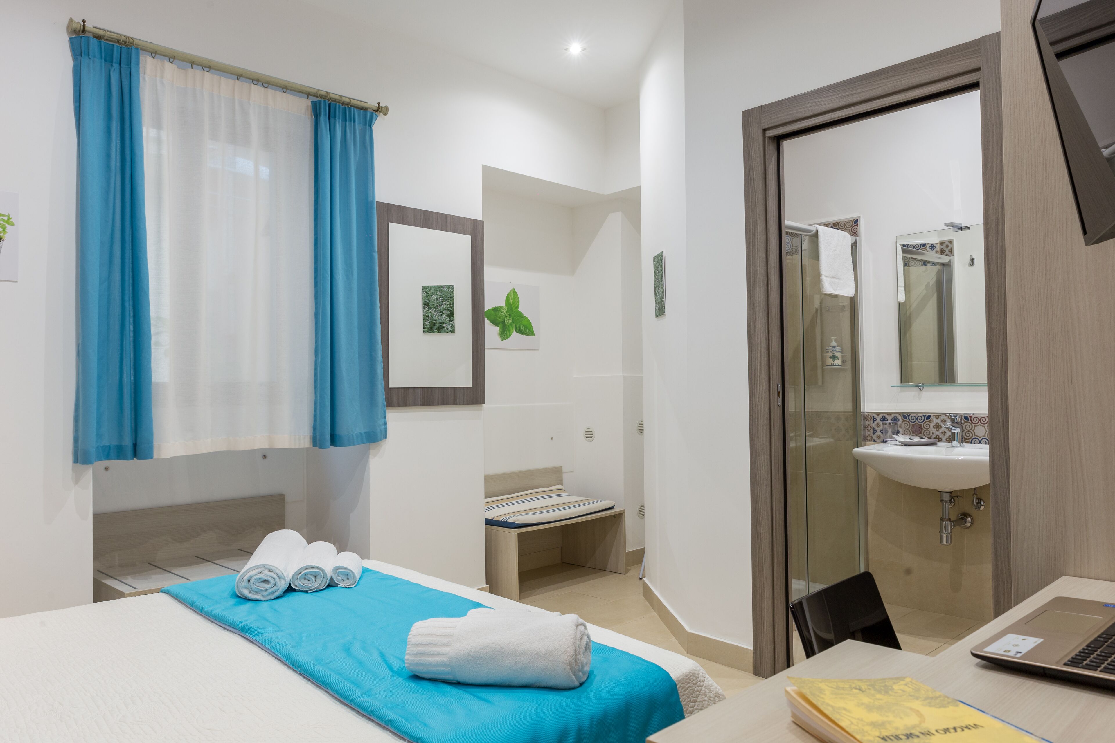 A hotel room with a bed, a desk with a laptop, a sink, and a shower area.