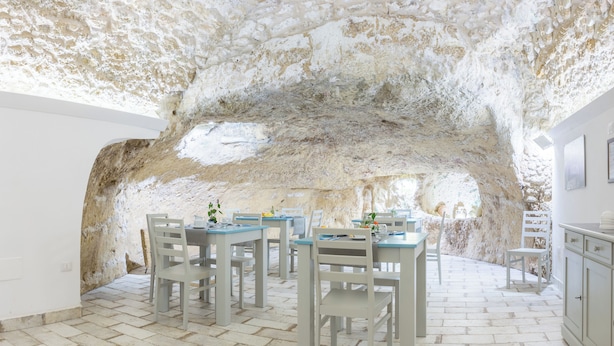 Un comedor con mesas y sillas, una pared de piedra y un piso blanco.
