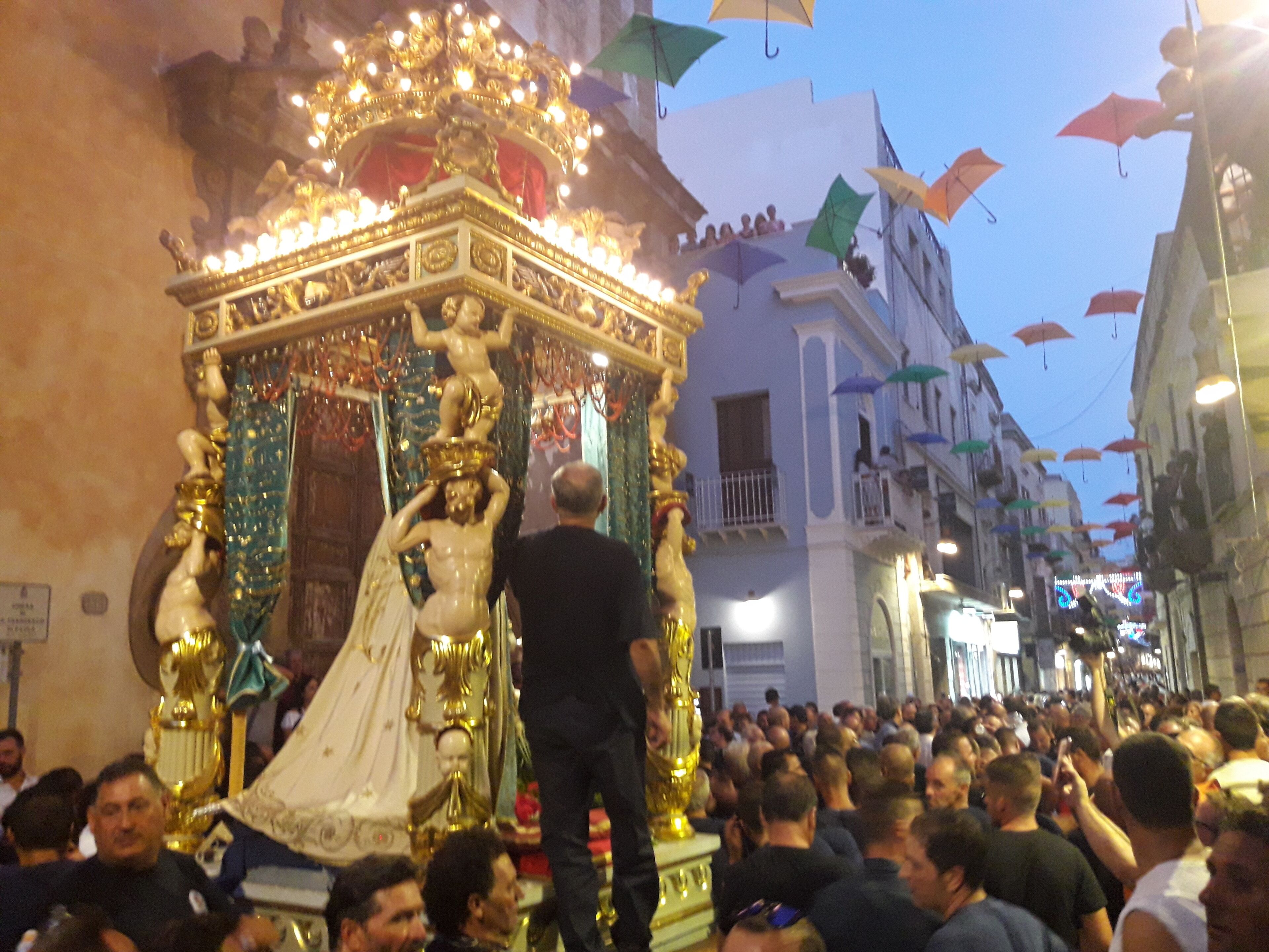 A crowded street with a golden ornate structure, possibly a religious icon, being carried by people.
