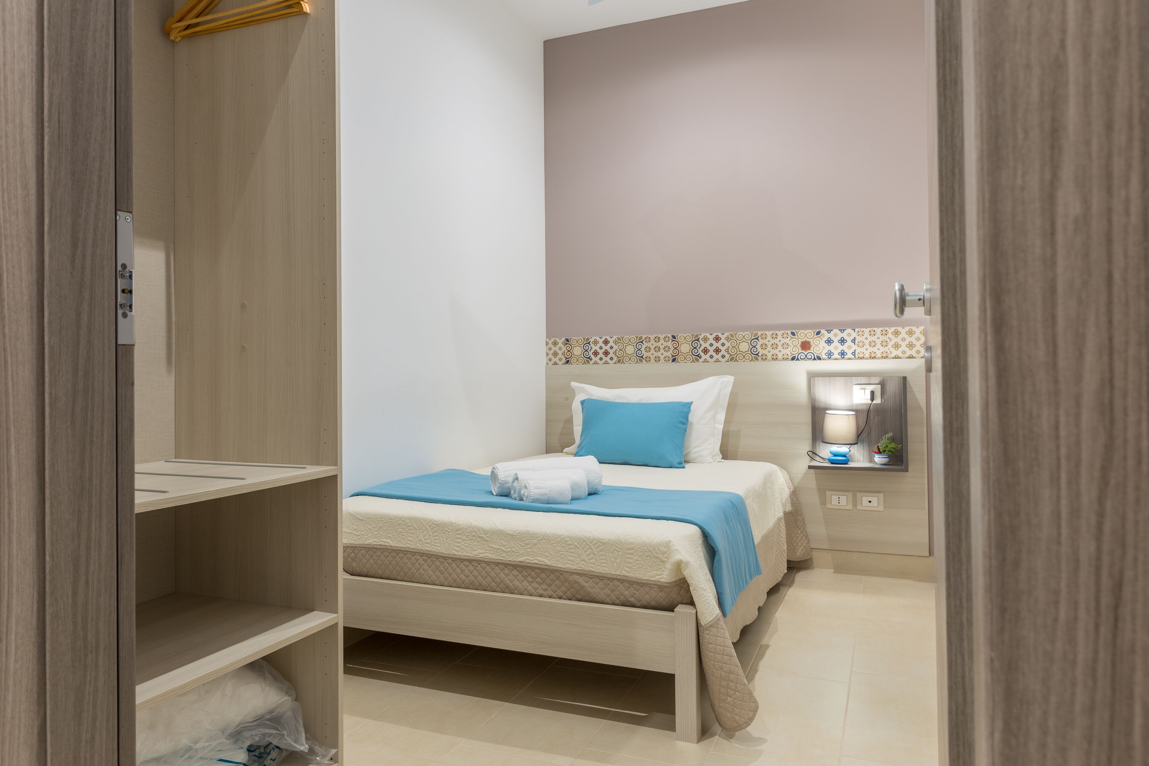 Ein Schlafzimmer mit einem Bett, einem Nachttisch, einer Lampe und einem an der Wand befestigten Regal.