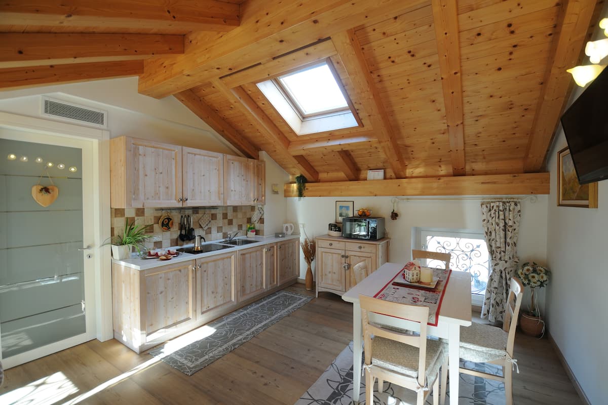 Une cuisine avec des meubles en bois, une table à manger avec des chaises et une lucarne.