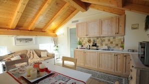 Una cocina acogedora con armarios de madera, un comedor con mesa lista para dos personas y una sala de estar con sofá y chimenea.