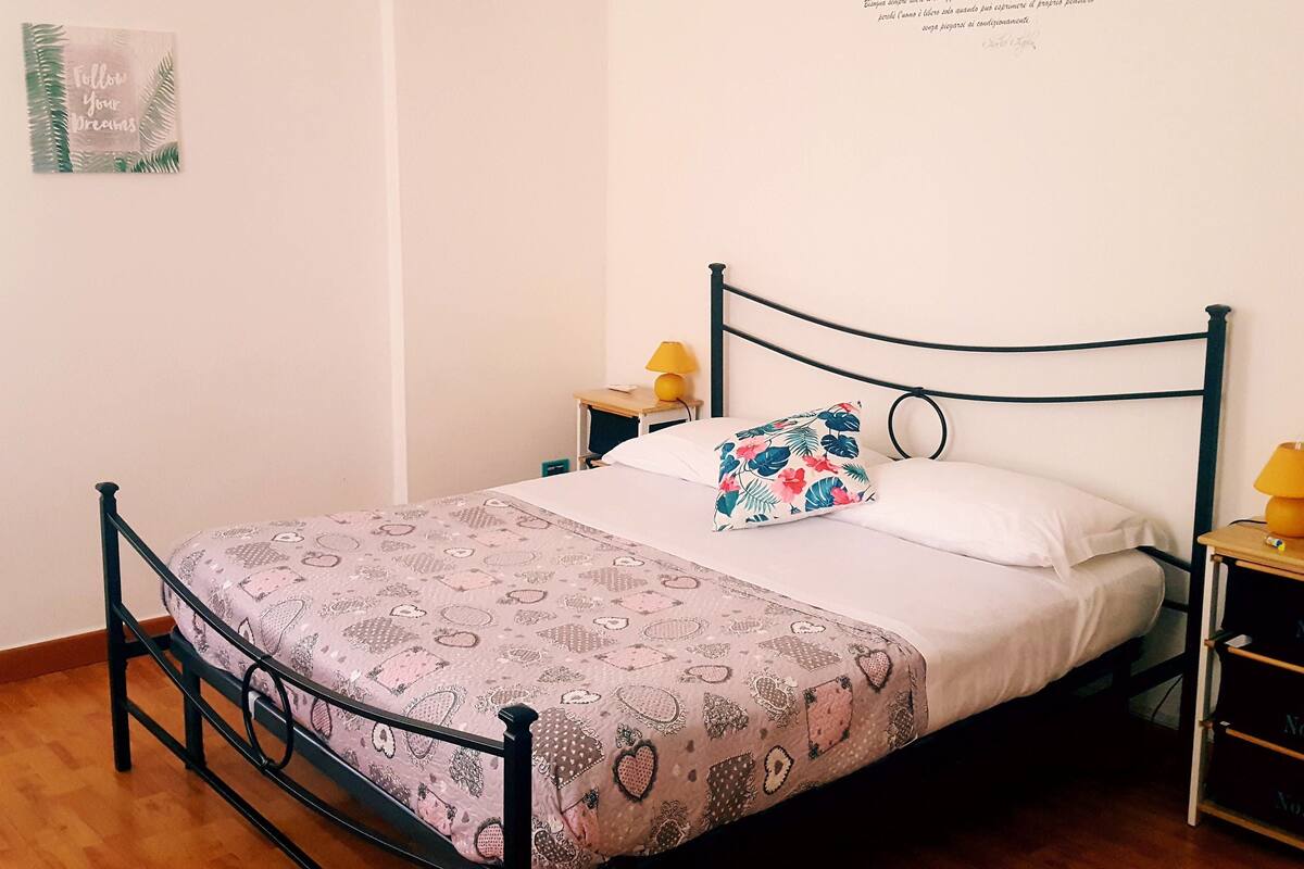 A neatly made bed with a patterned bedspread, a single decorative pillow, and a wall-mounted text.
