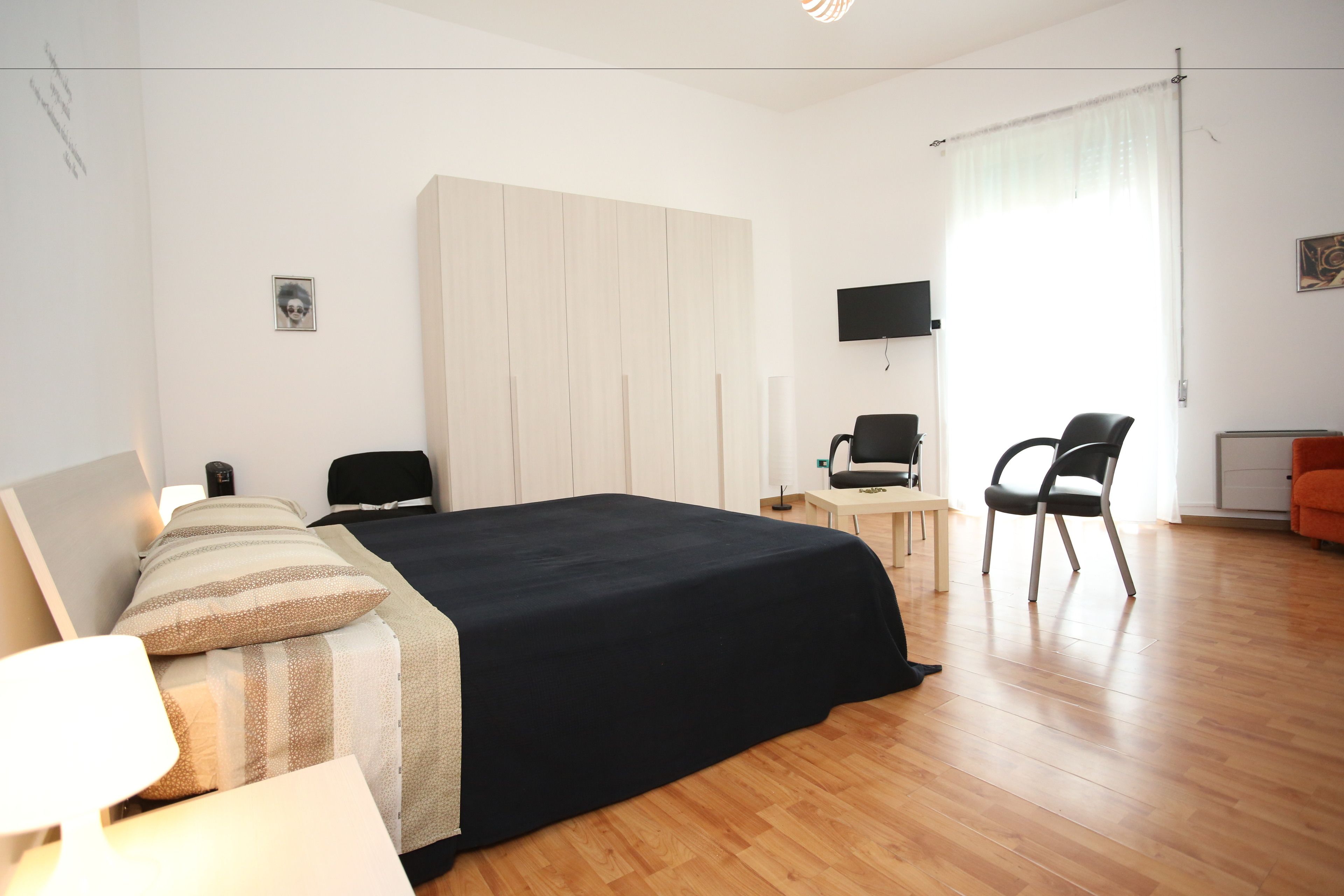 A modern bedroom with a large bed, a desk, a chair, and a TV on the wall.