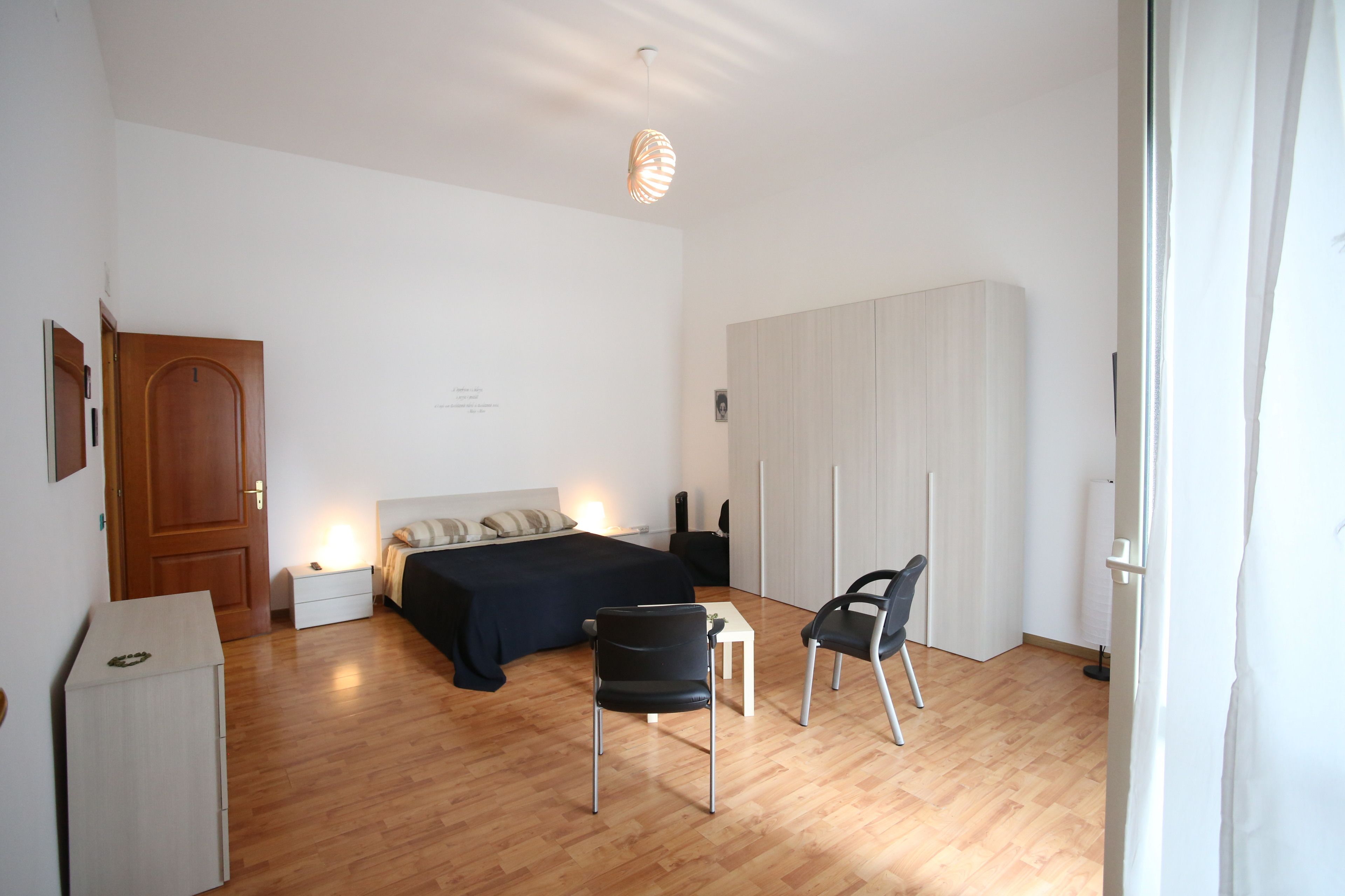 A bedroom with a bed, bedside table, chair, wardrobe, and a desk.
