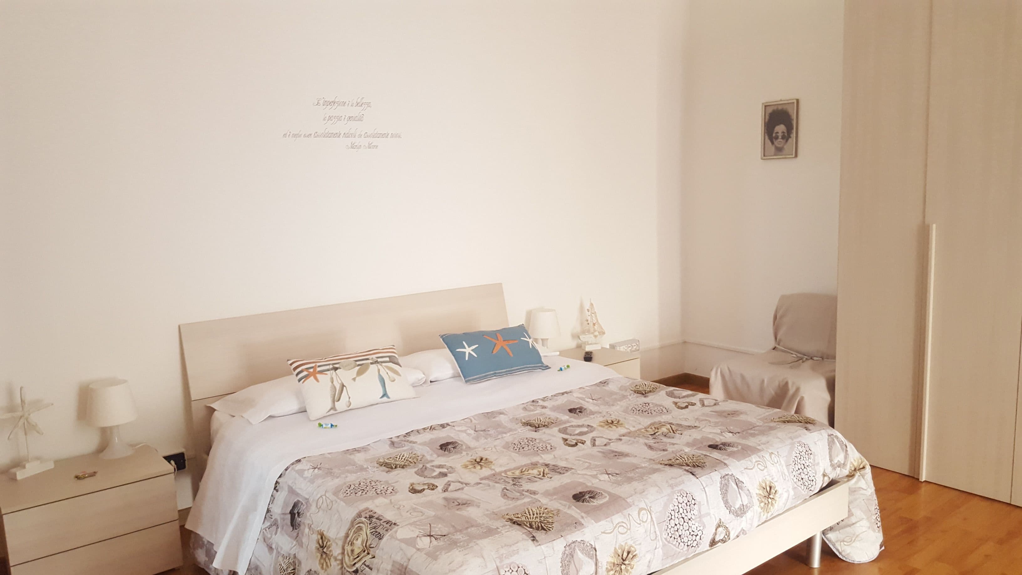 Une chambre bien rangée, avec un lit, des tables de chevet, une chaise et un tableau accroché au mur.