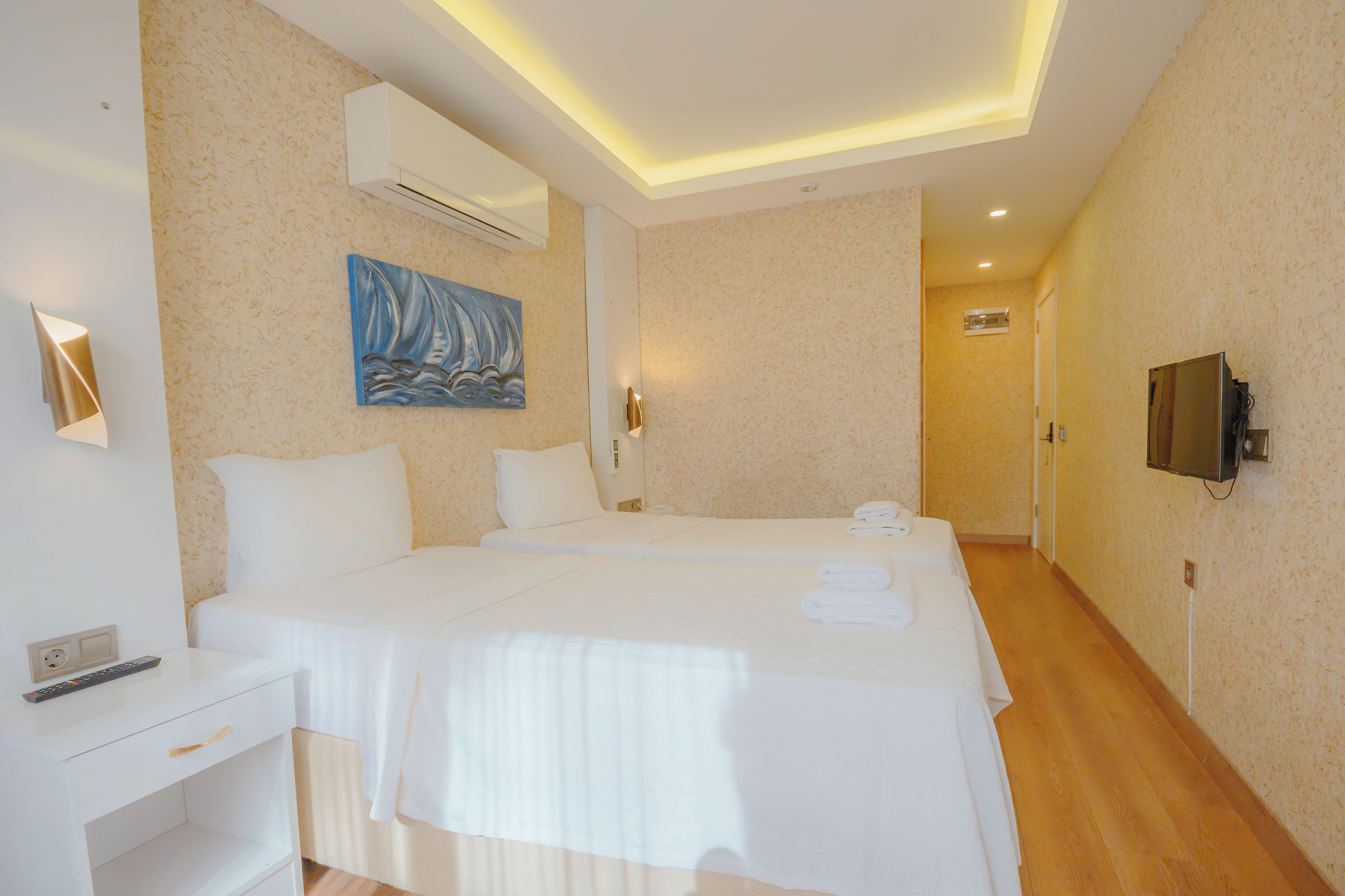 Une chambre d’hôtel avec deux lits, un tableau, un climatiseur, une télévision et un bureau avec une télécommande.