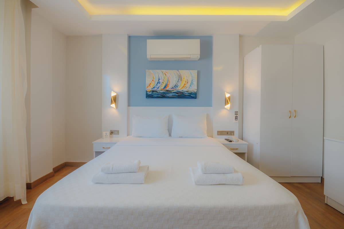 A modern hotel room with a large bed, two bedside tables, a wardrobe, and a ceiling-mounted air conditioner.