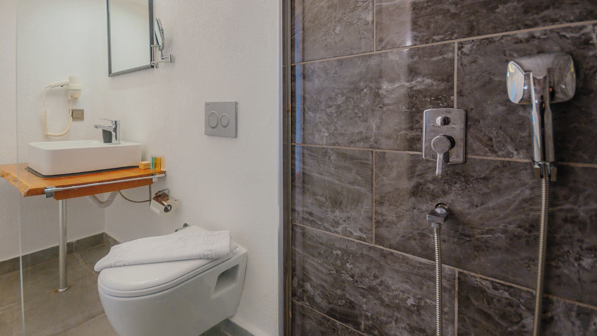 A bathroom with a white toilet, a sink with a mirror, and a shower area with a marble wall.