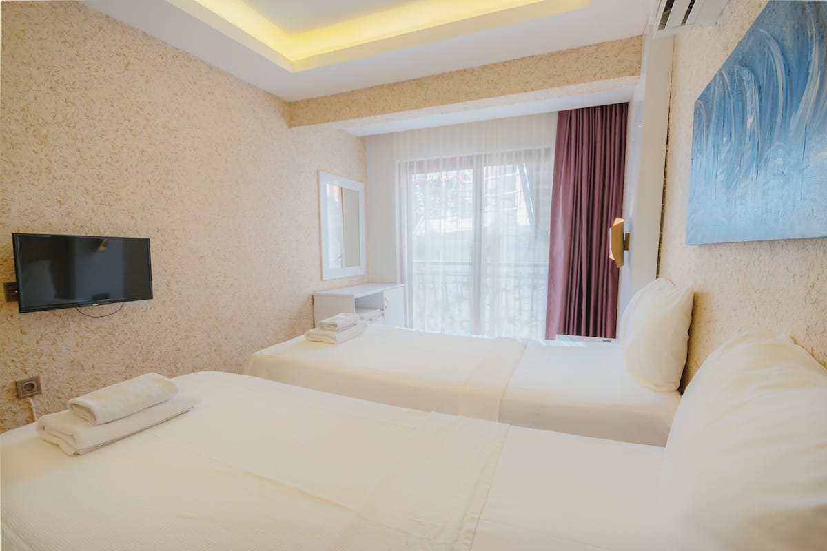 A hotel room with two beds, a flat-screen TV mounted on the wall, a window with curtains, and a painting on the wall.