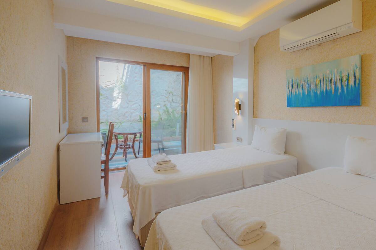 A hotel room with two beds, a TV, a painting, and a balcony with a chair.
