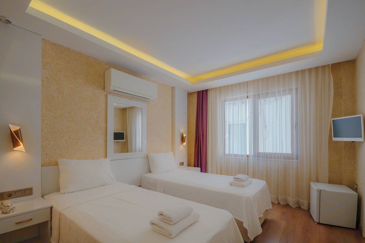 A hotel room with two beds, a TV, a small fridge, and a window with curtains.