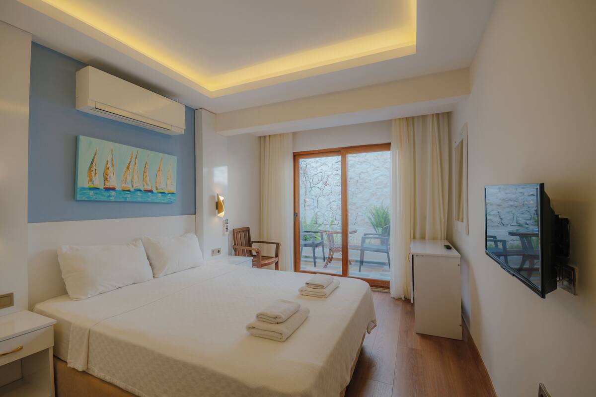 A hotel room with a bed, a desk, a chair, a TV, and a balcony with a table and chairs.