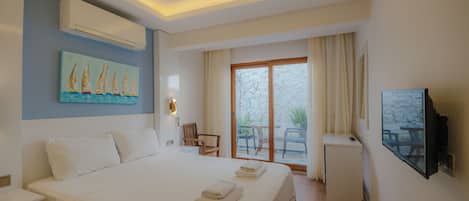 Habitación de hotel con cama, escritorio, silla, televisor y balcón con mesa y sillas.