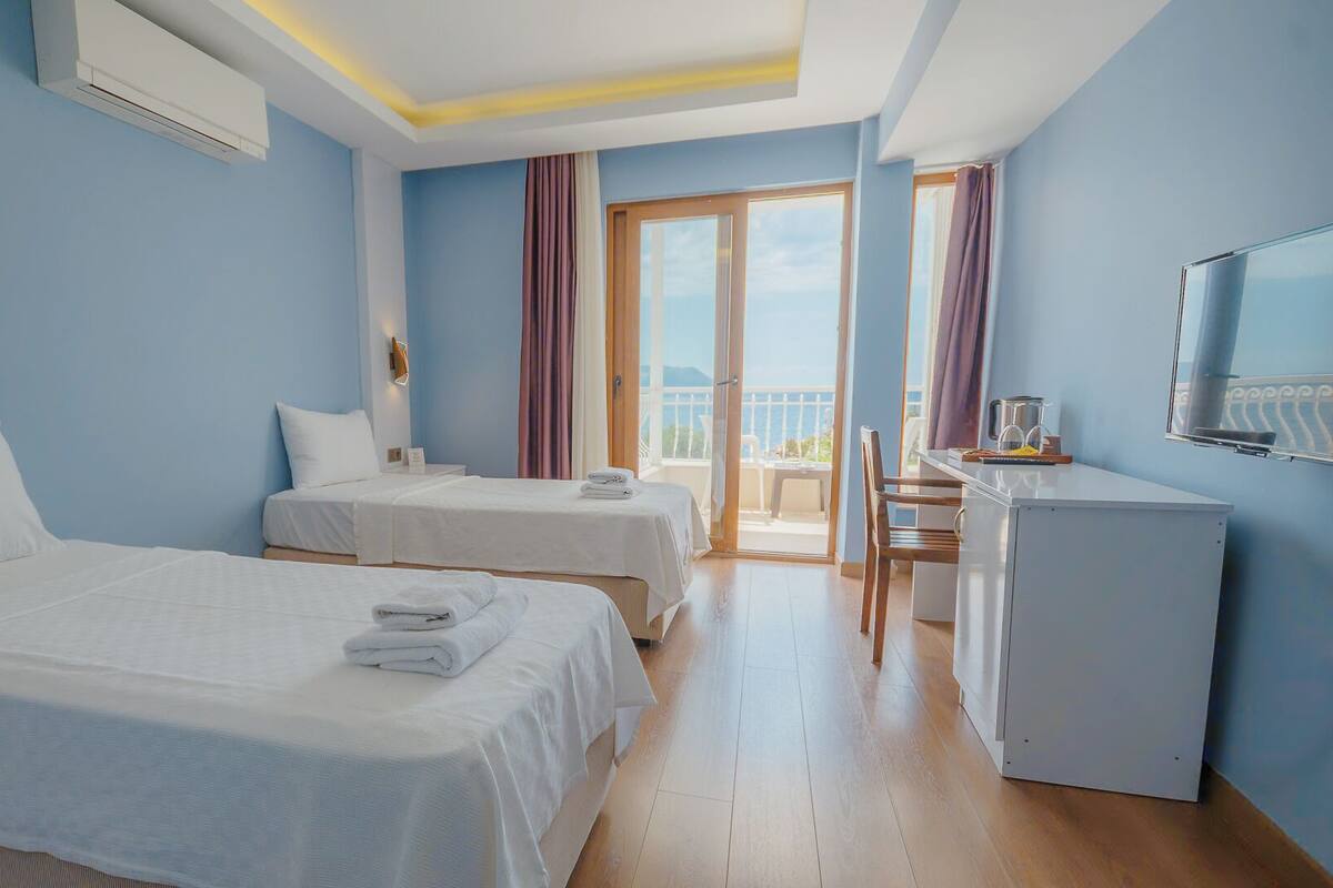 A hotel room with two beds, a desk, a TV, and a balcony with a view.