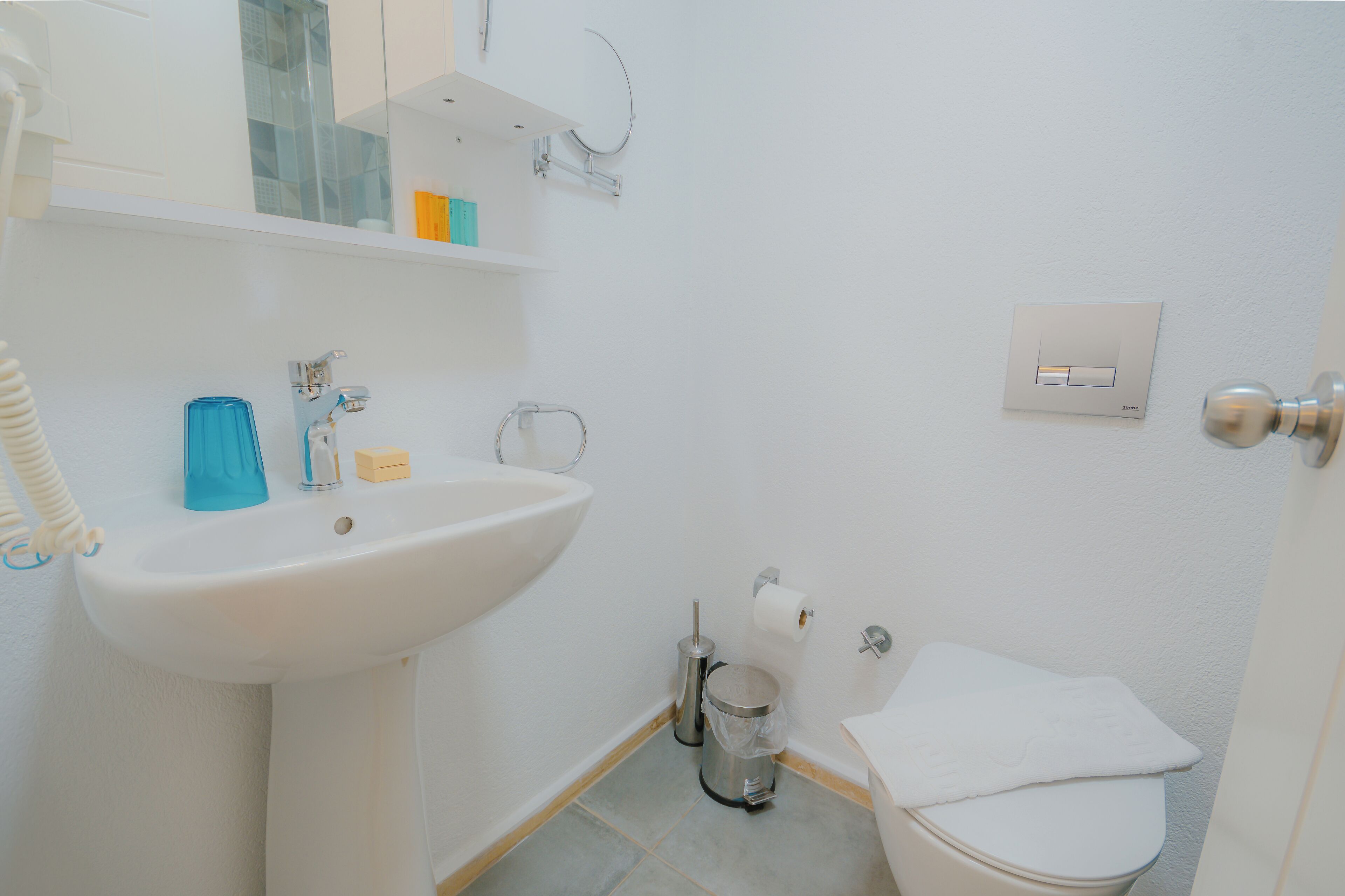 A small, clean bathroom with a white sink, toilet, and a shelf above the sink.