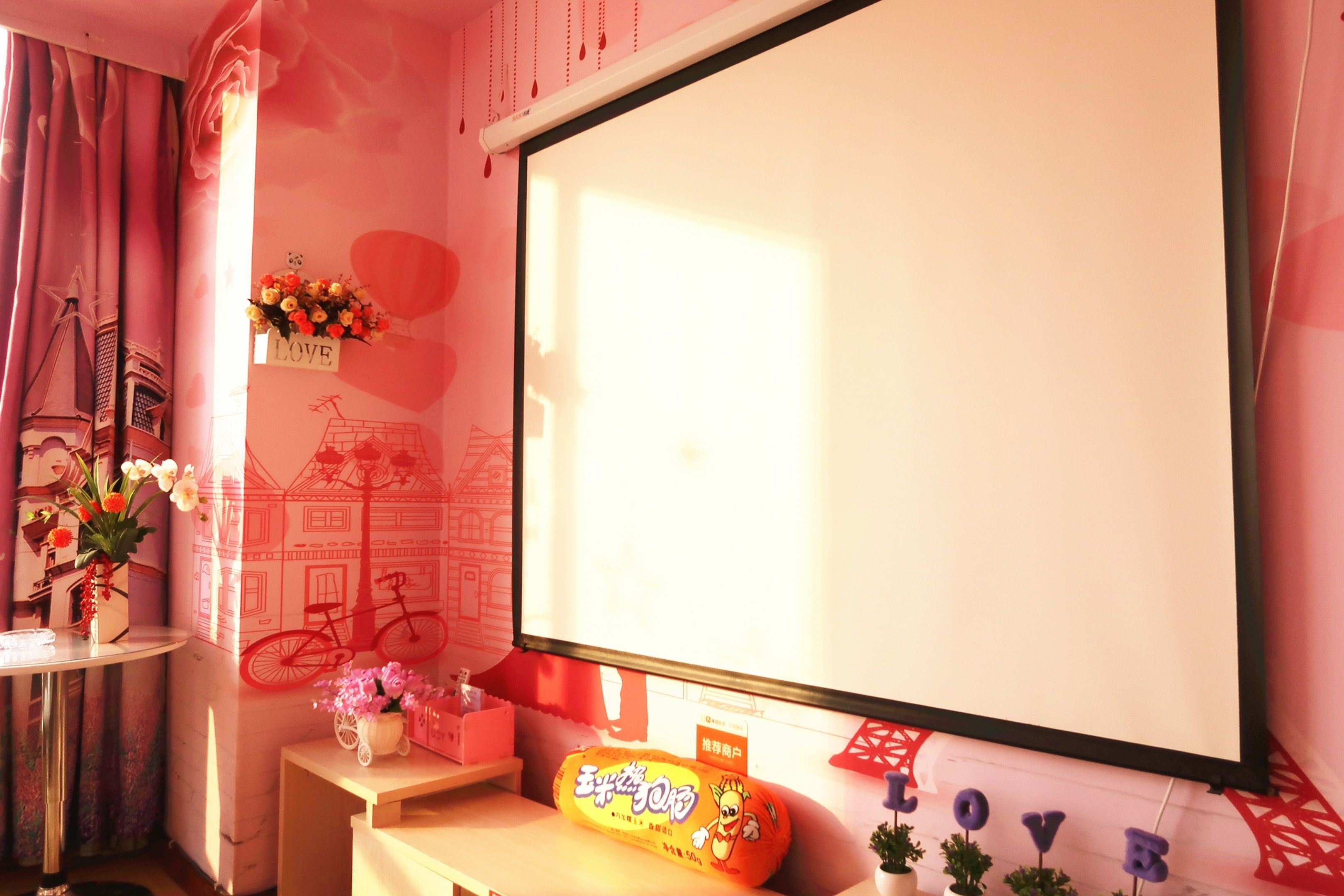 A room with a large window, a whiteboard, and a small table with a flower vase and a snack package.