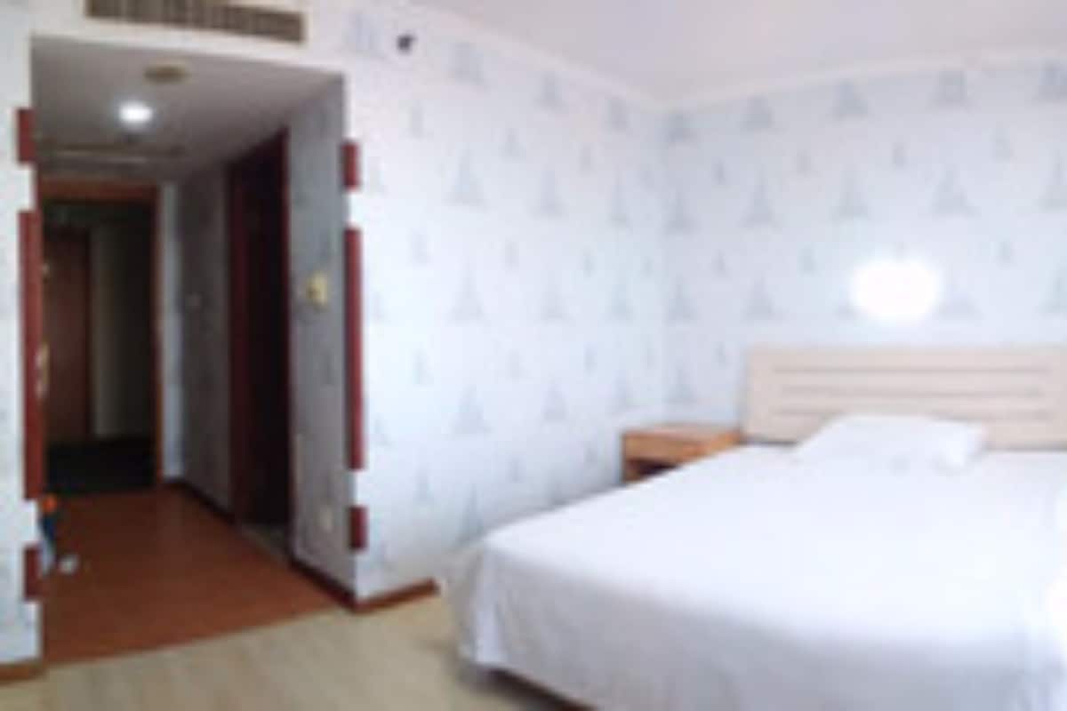 Quarto de hotel com cama, mesa de cabeceira e porta que dá para outro quarto.