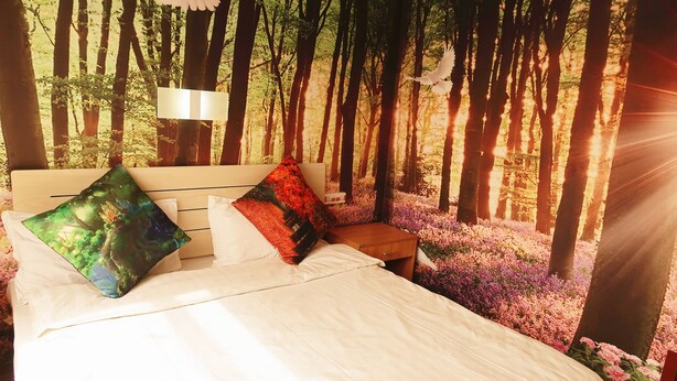 Une chambre à coucher avec un lit, des oreillers, une table de chevet et une fresque murale représentant une scène de forêt.