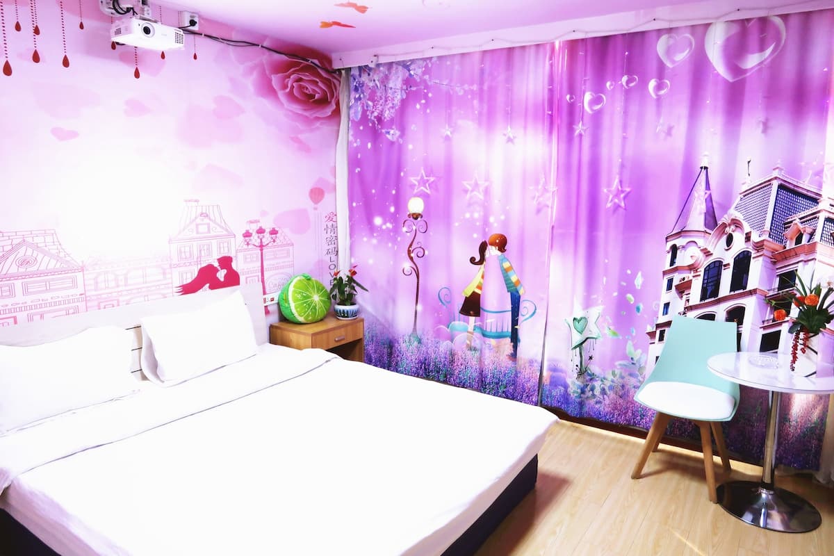 Um quarto com cama, mesa de cabeceira, cadeira e mesa.