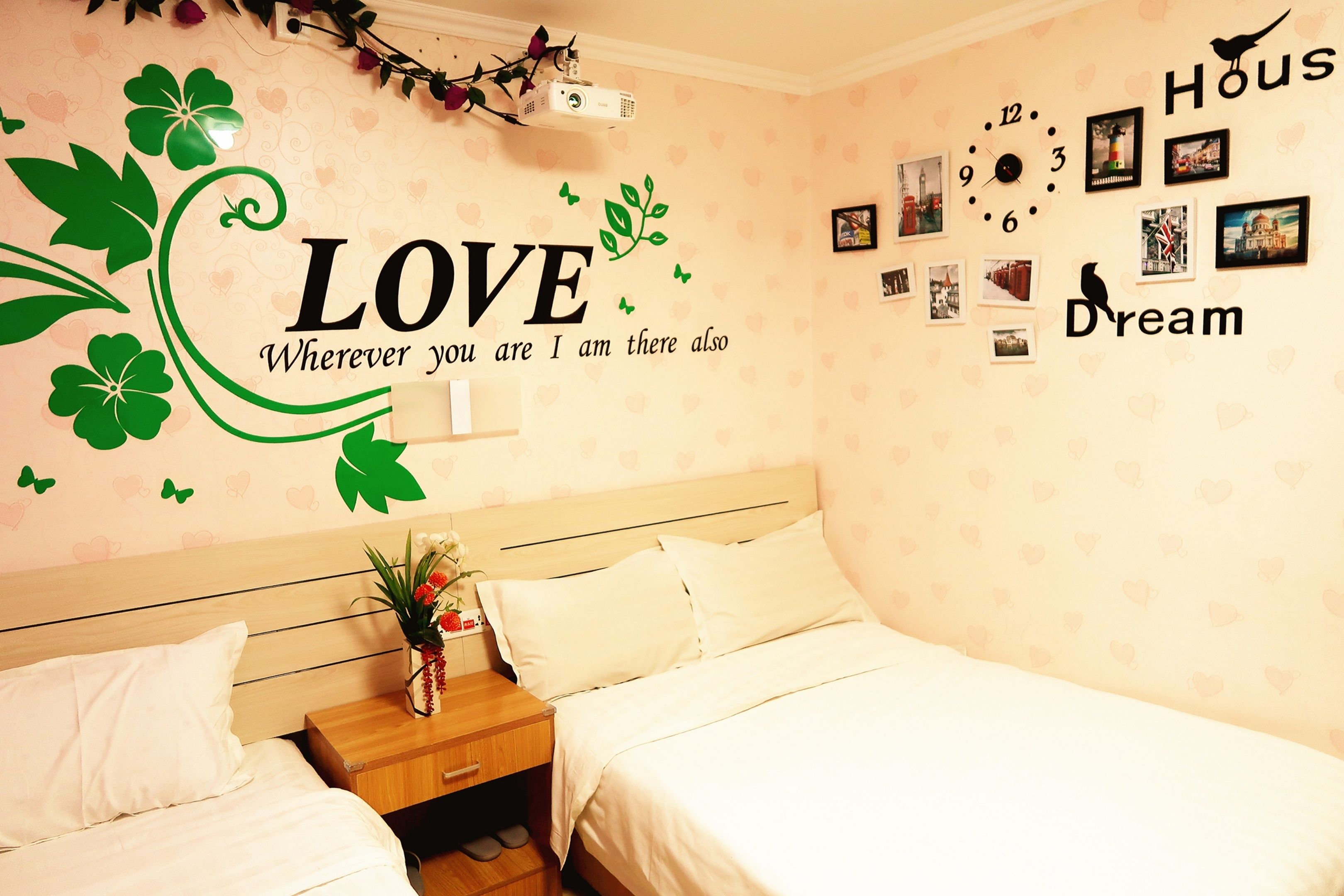 Un dormitorio con cama, mesita de noche y pared decorada con un vinilo con la palabra 'LOVE' y fotografías.