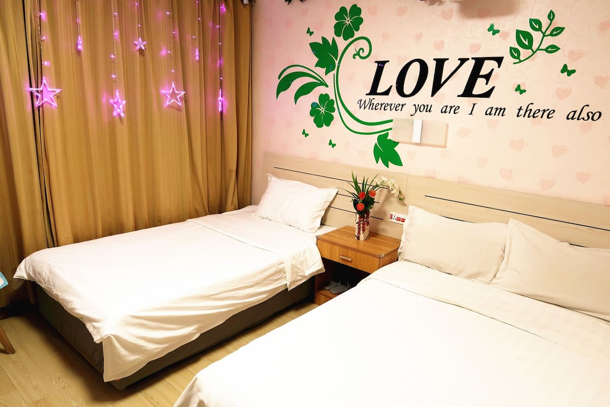 Quarto de hotel com duas camas, uma mesa de cabeceira com um vaso de flores e um adorno na parede com a palavra 'LOVE' e um desenho floral.