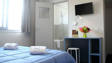A hotel room with a bed, a shower, a TV, and a small table with a vase of flowers.