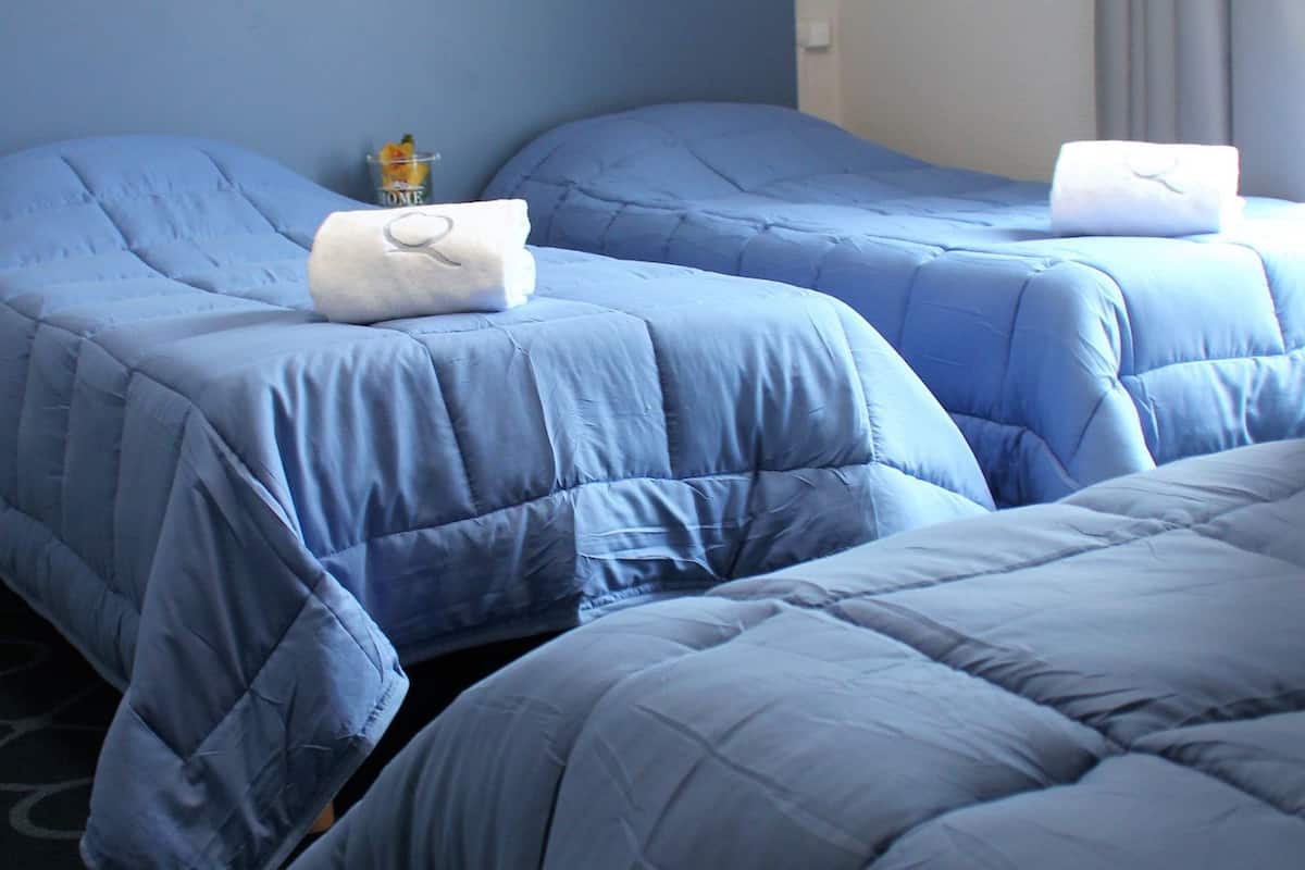 Quarto de hotel com duas camas, cada uma com um edredom azul e uma almofada branca.