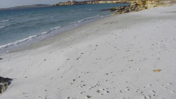 A beach with clear blue water, sandy shore, and rocky cliffs in the background. - Sardinia International House (Zeddiani)